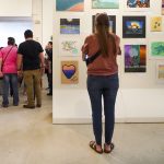 young woman stands with her back to camera in front of a wall filled with color youth art