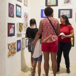 child locks arms around tall female family member as they look upon colorful youth art